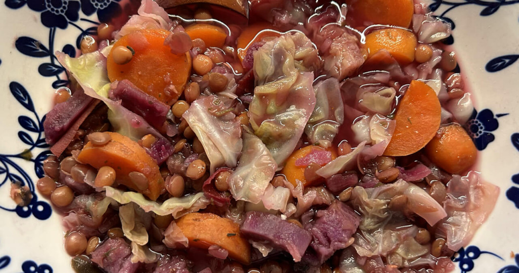 a photo of a big bowl of soup that contains lentils, purple sweet potato, carrots and cabbage