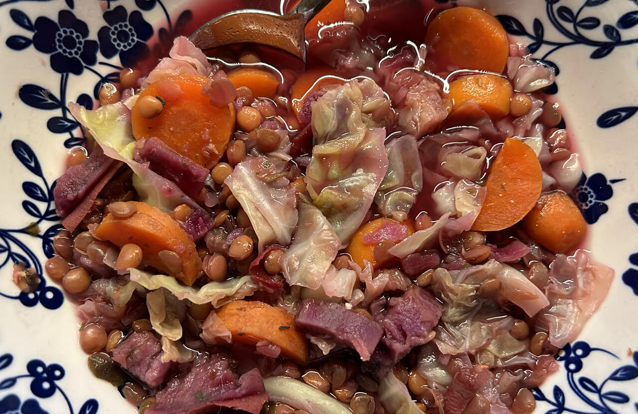 a photo of a big bowl of soup that contains lentils, purple sweet potato, carrots and cabbage